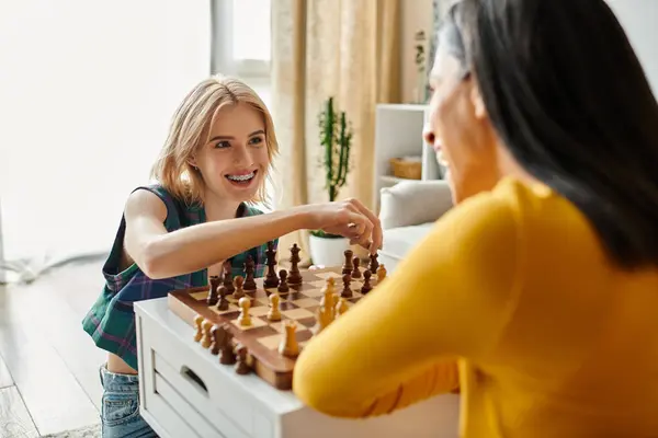 Две женщины улыбаются и веселятся, играя дома в шахматы в солнечный день. — стоковое фото
