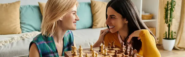 Две молодые женщины делятся улыбками и игривыми шутками, играя в шахматы в своей уютной гостиной. — стоковое фото