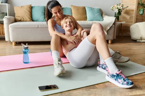 Dos mujeres jóvenes comparten un momento alegre e íntimo en colchonetas de ejercicio mientras disfrutan de su entrenamiento. - foto de stock
