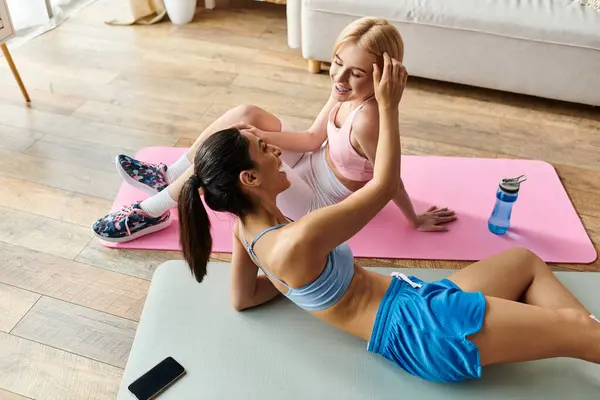 Dos mujeres jóvenes comparten risas y momentos cariñosos mientras hacen ejercicio juntas en casa. - foto de stock