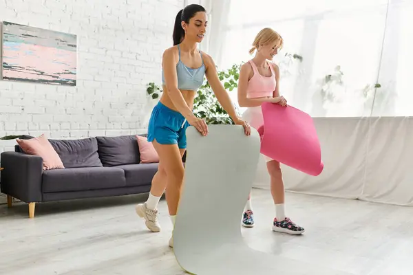 Two loving women roll out exercise mats in their stylish living space, ready for a fun workout. — Stockfoto