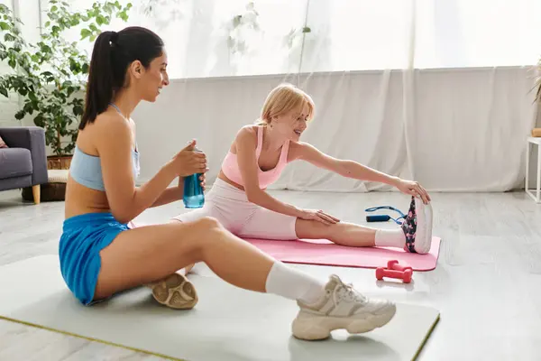 Two young women engage in a loving workout while stretching together on mats. — Stock Photo