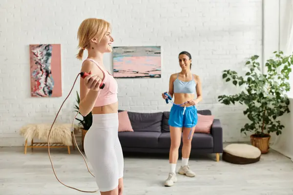 Two young women enjoy a playful workout, laughing together in their cozy living space. — Stock Photo