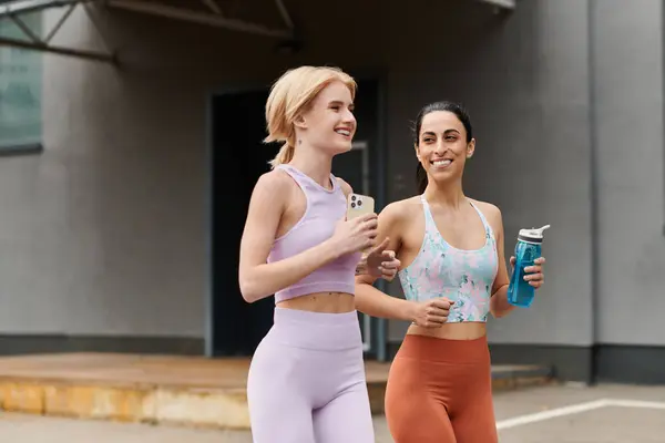 Two young women laugh and share a moment while jogging in athletic wear, embracing their bond. — Stock Photo