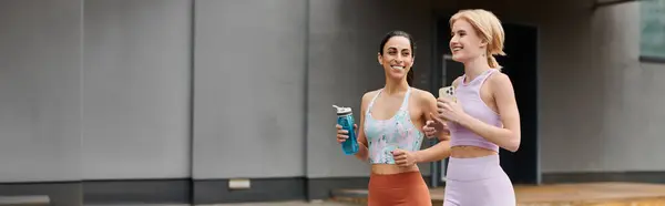 Two young women share smiles and drinks, celebrating their fitness and love outdoors. — Stock Photo
