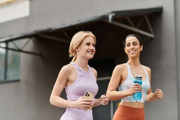 Two young women run side by side, smiling and sharing a moment of joy outdoors while exercising. — Stock Photo