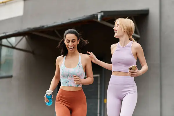 Two young women run and laugh together, celebrating love and fitness on a sunny day. — Stock Photo