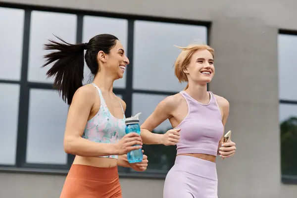 Two young women laugh and enjoy a run together in a vibrant city, showcasing their bond. — Stock Photo