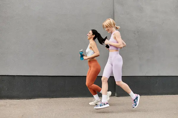 Two vibrant women jog side by side, sharing laughter and happiness in a park setting. — Stock Photo