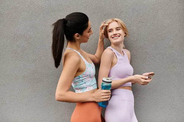 Two young women share laughter and affection while standing next to a wall, brightening the day. — Stock Photo