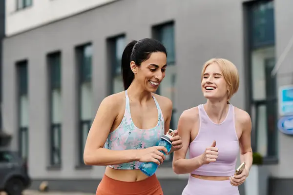 Two young women share laughter and joy while jogging through an urban setting. — Stock Photo