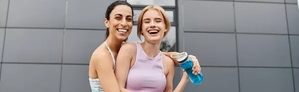 Two young women embrace each other with big smiles at the gym, showing their affection. — Stockfoto