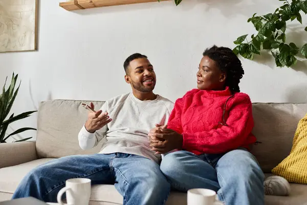 A joyful African American couple relaxes on their sofa, enjoying a cozy winter day together. — Stock Photo