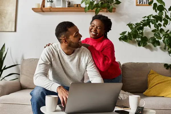 A happy couple embraces a cozy winter day together in their warm living room, man working remotely on laptop — Stock Photo