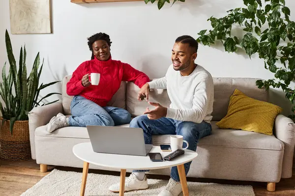 A loving couple relaxes on a couch, enjoying warm drinks and each others company indoors. — Stock Photo