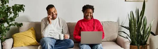 Happy couple laughs and works on a laptop together in their cozy living room. — Stock Photo