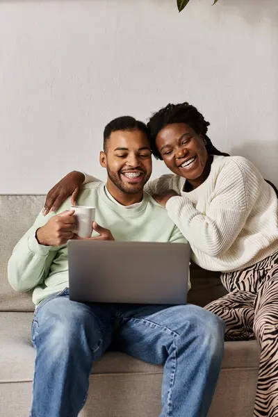 A joyful couple enjoys quality time together on a couch while using a laptop, staying warm. — Stock Photo