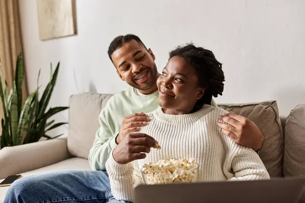 A happy couple shares a warm evening at home, wearing sweaters and savoring popcorn. — Stock Photo