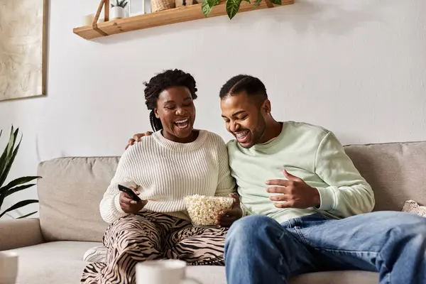 Una coppia felice si gode i popcorn mentre si coccola sul divano, abbracciando una calda serata invernale. — Foto stock