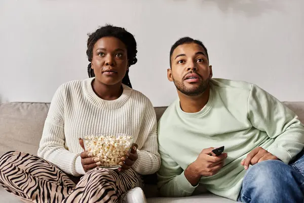 Una coppia felice si coccola sul divano, guardando un film e condividendo popcorn in maglioni accoglienti. — Foto stock