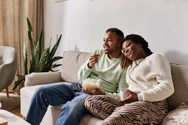 Una coppia felice si rilassa su un divano, condividendo spuntini e risate nel loro accogliente soggiorno. — Foto stock