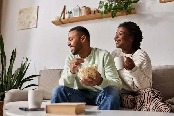 Coppia si rilassa sul divano, condividendo popcorn e calore durante una fredda serata invernale. — Foto stock