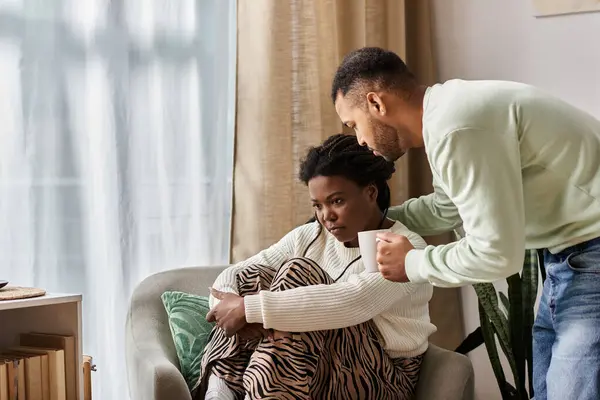 Afroamerikaner mit Tasse tröstet seine Partnerin in ihrem gemütlichen Wohnzimmer — Stockfoto