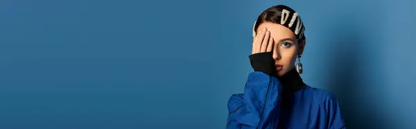 Young woman poses gracefully with hair clips, highlighting her stylish attire on a blue backdrop. — Stock Photo