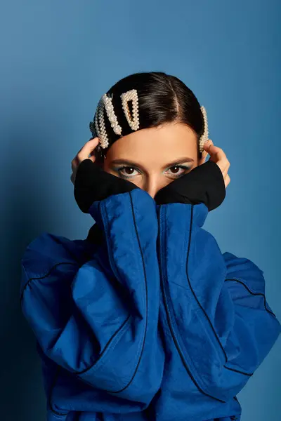 Young woman poses confidently in stylish attire with unique hair clips against a blue backdrop. — Stock Photo