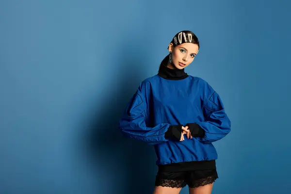 A stylish young woman displays her trendy outfit against a bold blue backdrop, exuding confidence. — Stock Photo