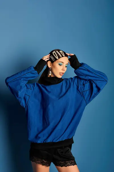 A fashionable young woman poses confidently in stylish attire against a blue backdrop. — Stock Photo