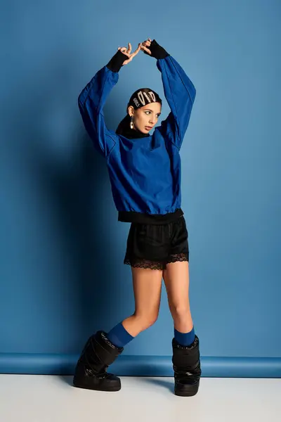 A chic woman poses confidently in stylish clothes against a vibrant blue backdrop. — Stock Photo