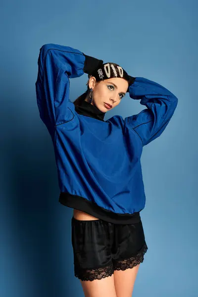 Charming young woman poses confidently in stylish attire against a blue backdrop. — Stock Photo