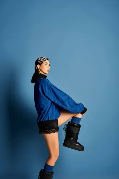 Una mujer joven y de moda muestra su atuendo de moda en un vibrante telón de fondo azul en un estudio. - foto de stock