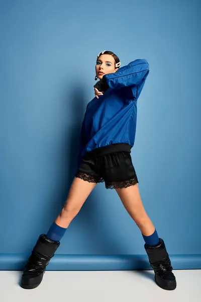 A trendy woman showcases her fashionable outfit while posing confidently on a blue background. — Stock Photo