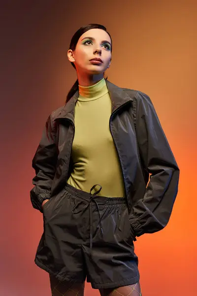 Una mujer joven posa con confianza en un atuendo de moda sobre un fondo de degradado naranja. - foto de stock