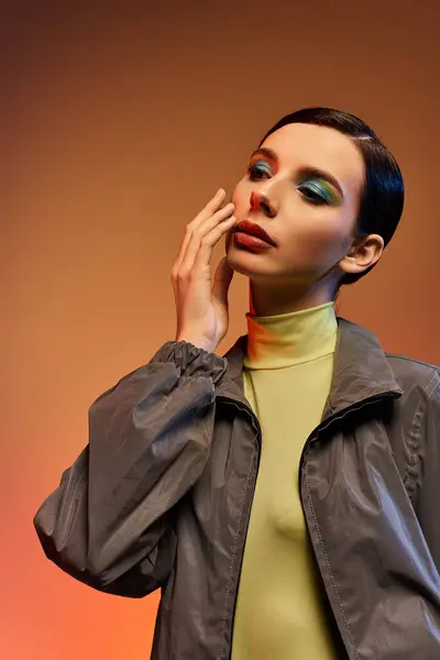 Uma jovem mulher elegante posa confiantemente em trajes da moda contra um cenário gradiente quente. — Fotografia de Stock