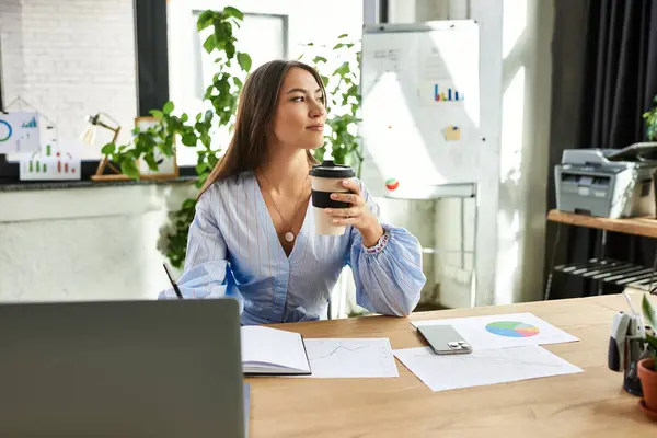 Belle brune réfléchit soigneusement avec du café, analysant des graphiques et des données à son bureau. — Photo de stock
