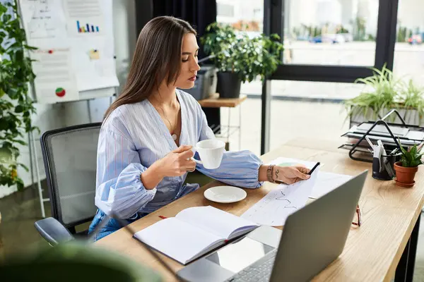 Brunette woman works intently in a bright, plant filled office with coffee in hand. — Stock Photo