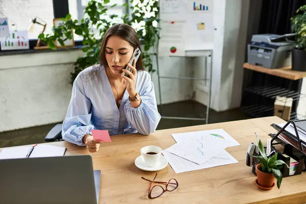 Joven morena en una llamada mientras maneja papeleo y café en su escritorio. - foto de stock