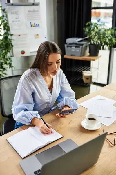 Brunette woman writing notes while using her smartphone in a stylish office environment — Stock Photo
