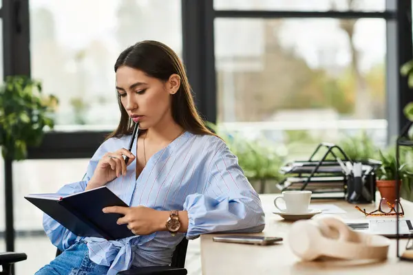 Brunette woman writes thoughtfully in a notebook while seated in a modern workspace. — Stock Photo