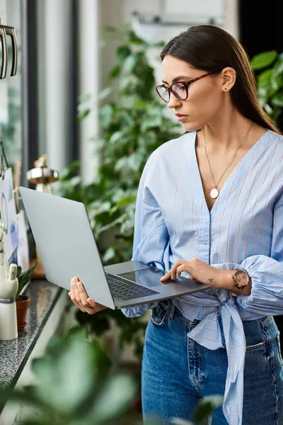 Brunette woman types intently on her laptop while surrounded by vibrant plants. — Stock Photo