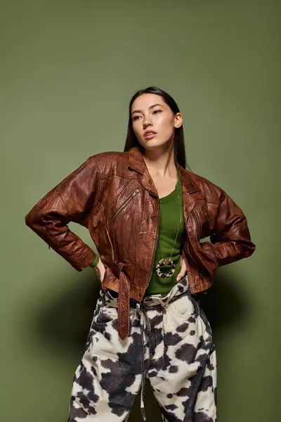 Confident young brunette woman showcases her fashion sense in a brown leather jacket while posing. — Stock Photo
