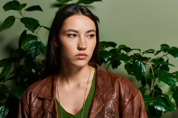 A young brunette woman thoughtfully gazes amid vibrant green leaves, exuding elegance. — Stock Photo