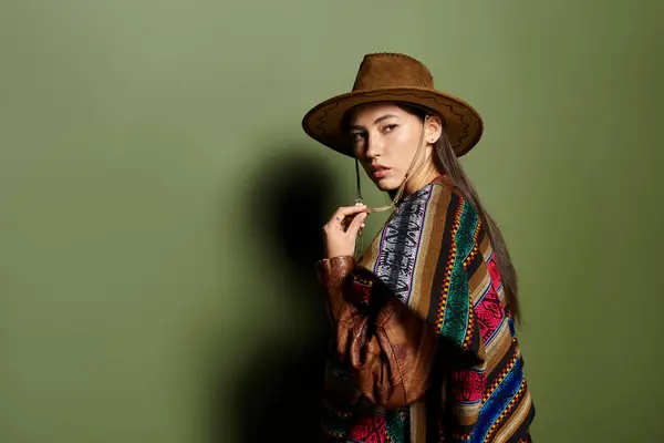 A charming young woman in a colorful poncho and hat stands out against a bold green backdrop. — Stock Photo