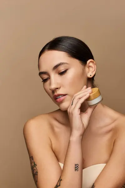 Bella giovane donna applica crema idratante mentre mette in evidenza la sua pelle radiosa in luce morbida — Foto stock