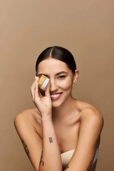 Brunette woman joyfully poses while showcasing a skincare product, exuding beauty and confidence. — Stock Photo