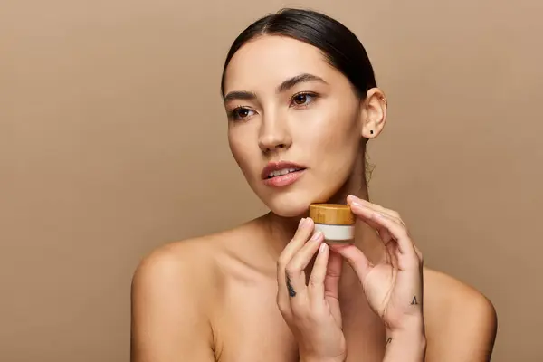 Jeune femme démontre la beauté naturelle tout en tenant un bocal de soins de la peau dans un cadre serein. — Photo de stock