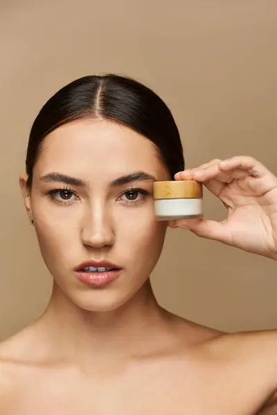 Young brunette woman holds a small skincare jar, promoting beauty and self care with elegance. — Stock Photo